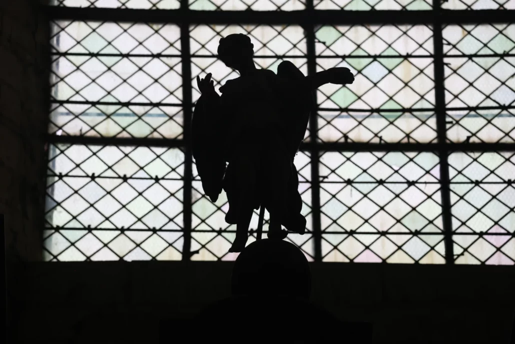 Statue d'ange en contre-jour devant un vitrail dans une église de l'Auxerrois